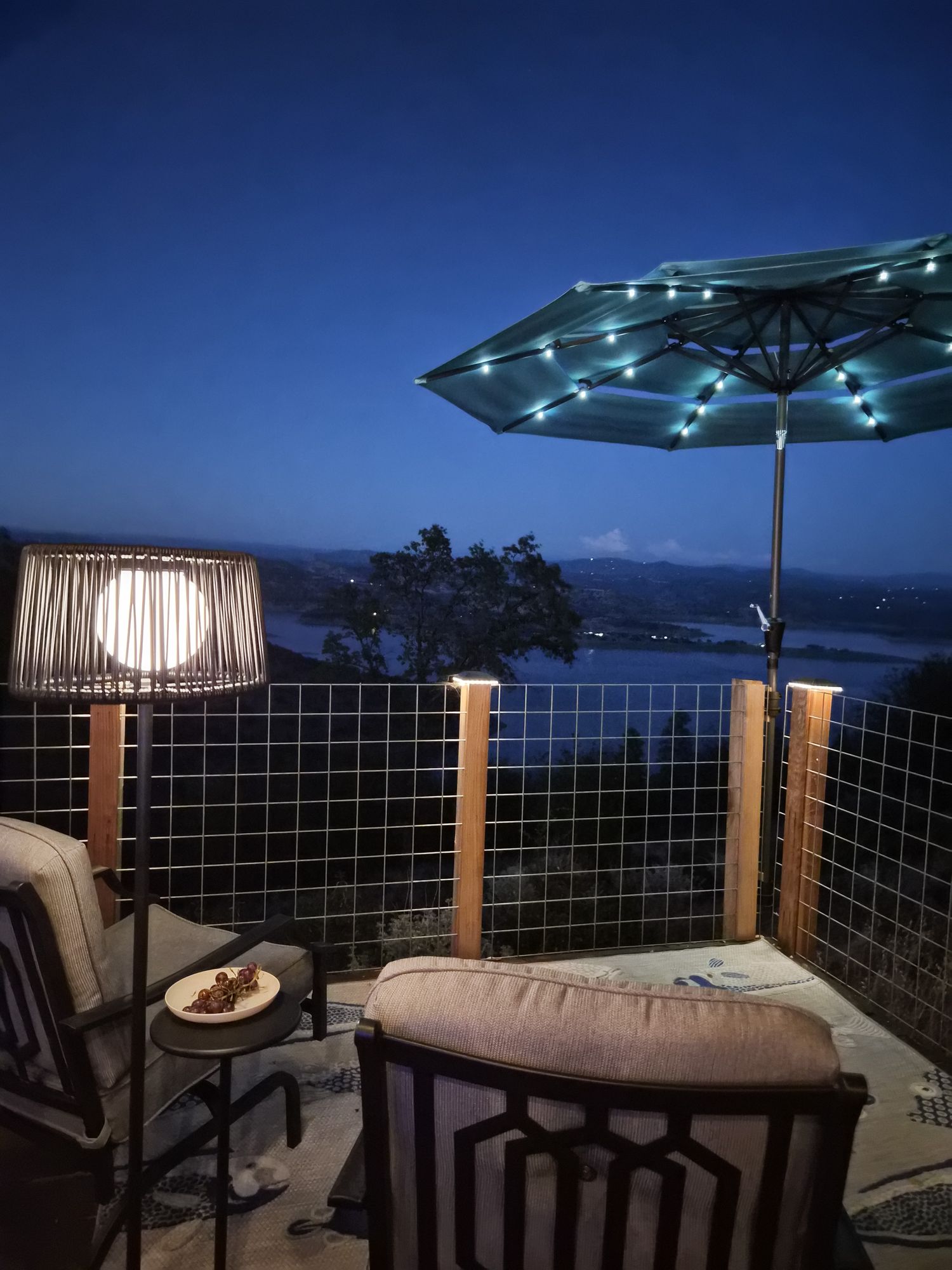 Lounge chairs under a lit umbrella, lake at blue hour